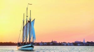 sailboat on the ocean, buildings in the back at sunset