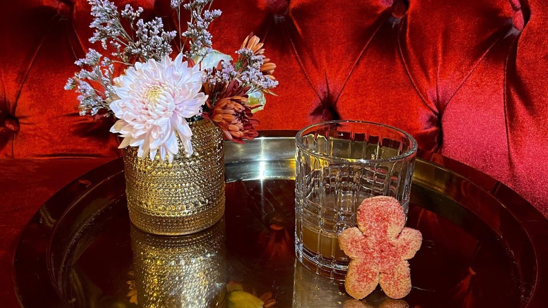 alcoholic drink on a tray with gingerbread candy and flower vase beside it