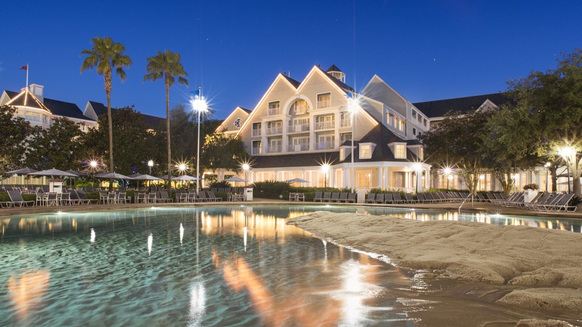 hotel with pool in front and sand, pool chairs at the side and trees