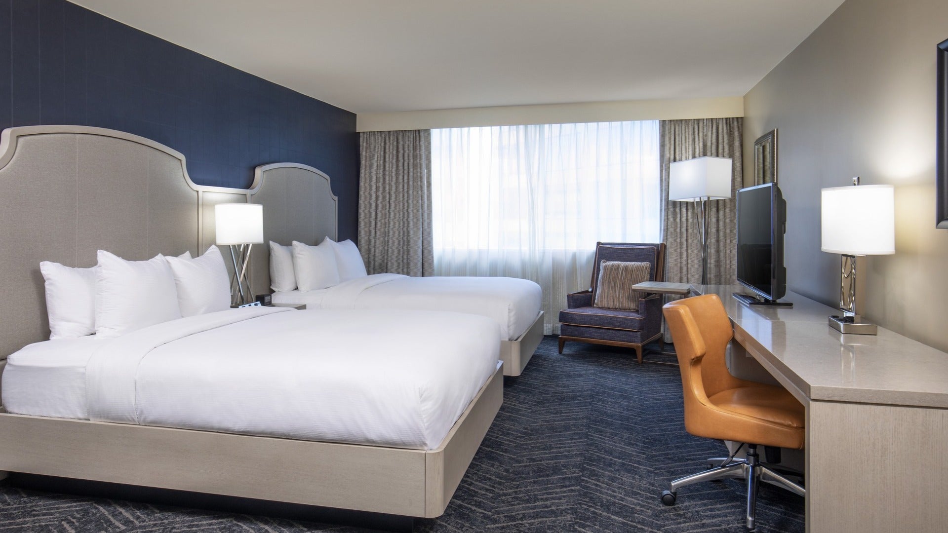 hotel room with two beds, chairs, lamps, and curtains