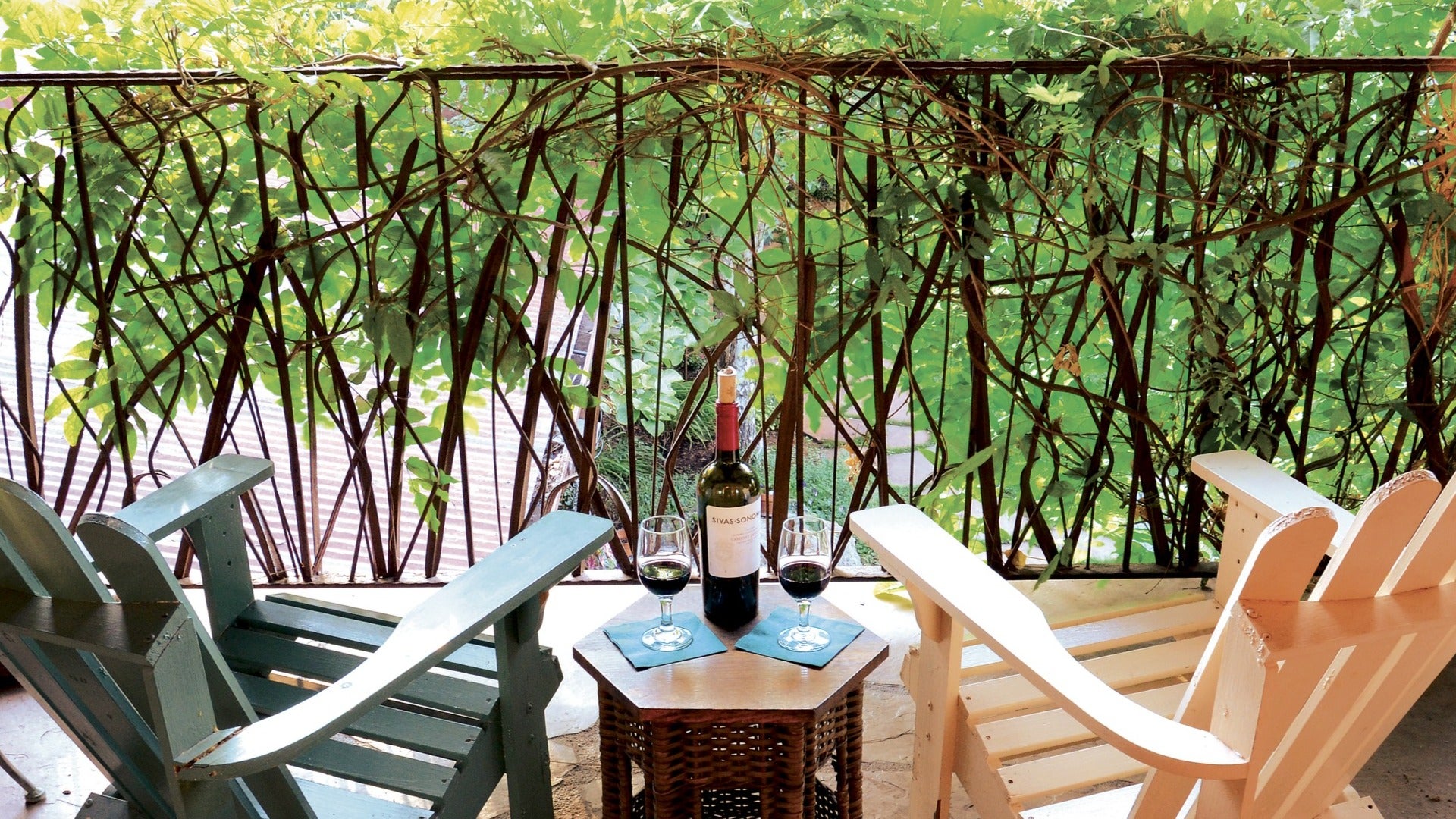 outdoor chairs with a table, wine, and wine glasses in a balcony