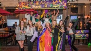 group of people enjoying drinks on a street, mardi gras sign at the back