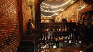 people drinking in a speakeasy, with a display of alcohol in front and string lights on the ceiling