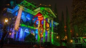 haunted mansion with pumpkin scarecrow in front and trees surrounding it