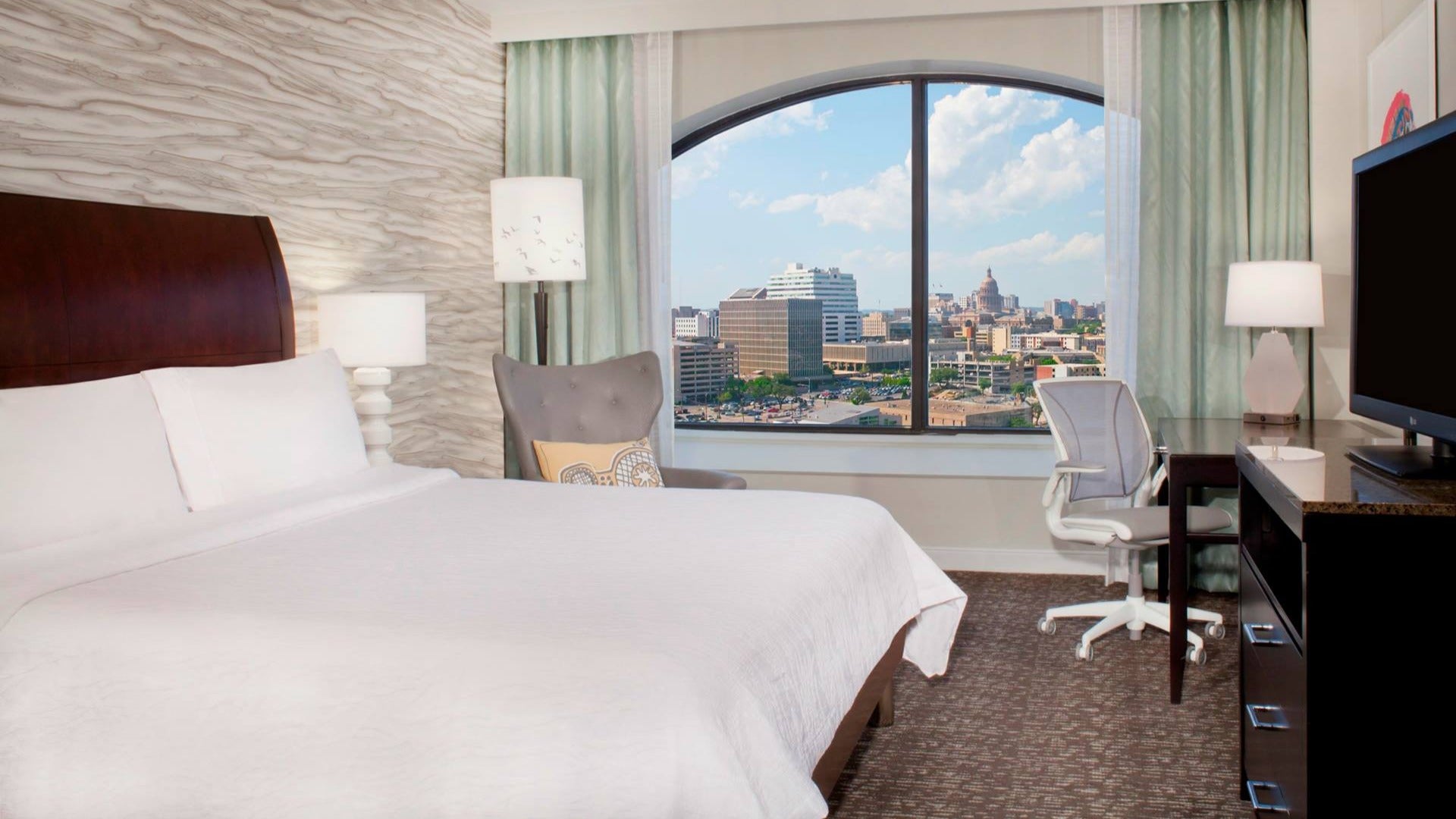 hotel room with bed, chairs, window and view of city