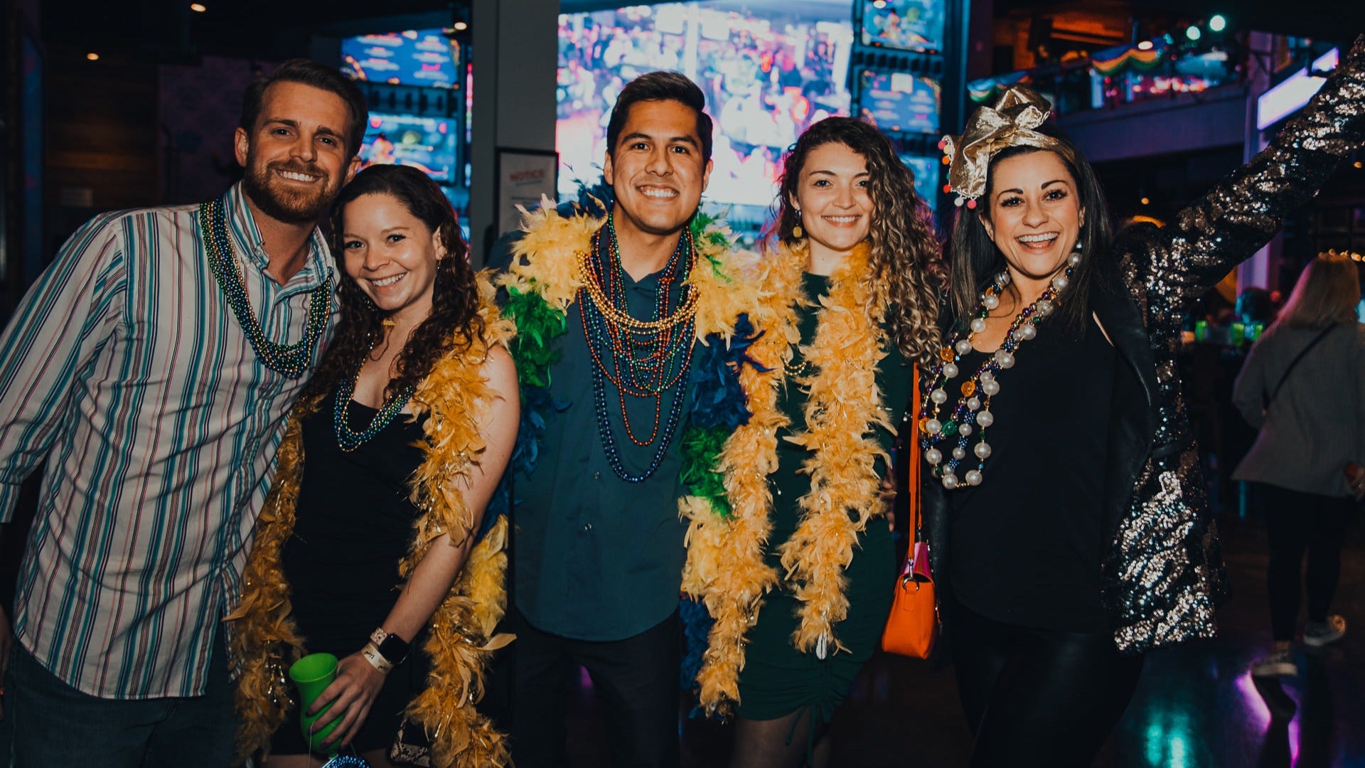 group of people in mardi gras attire with beads and screen at the back