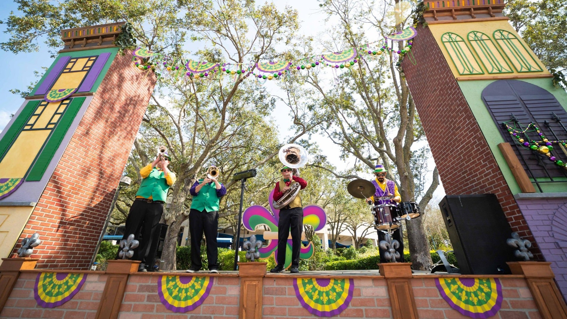 group of performers with instruments on a stage during mardi gras, trees at the back