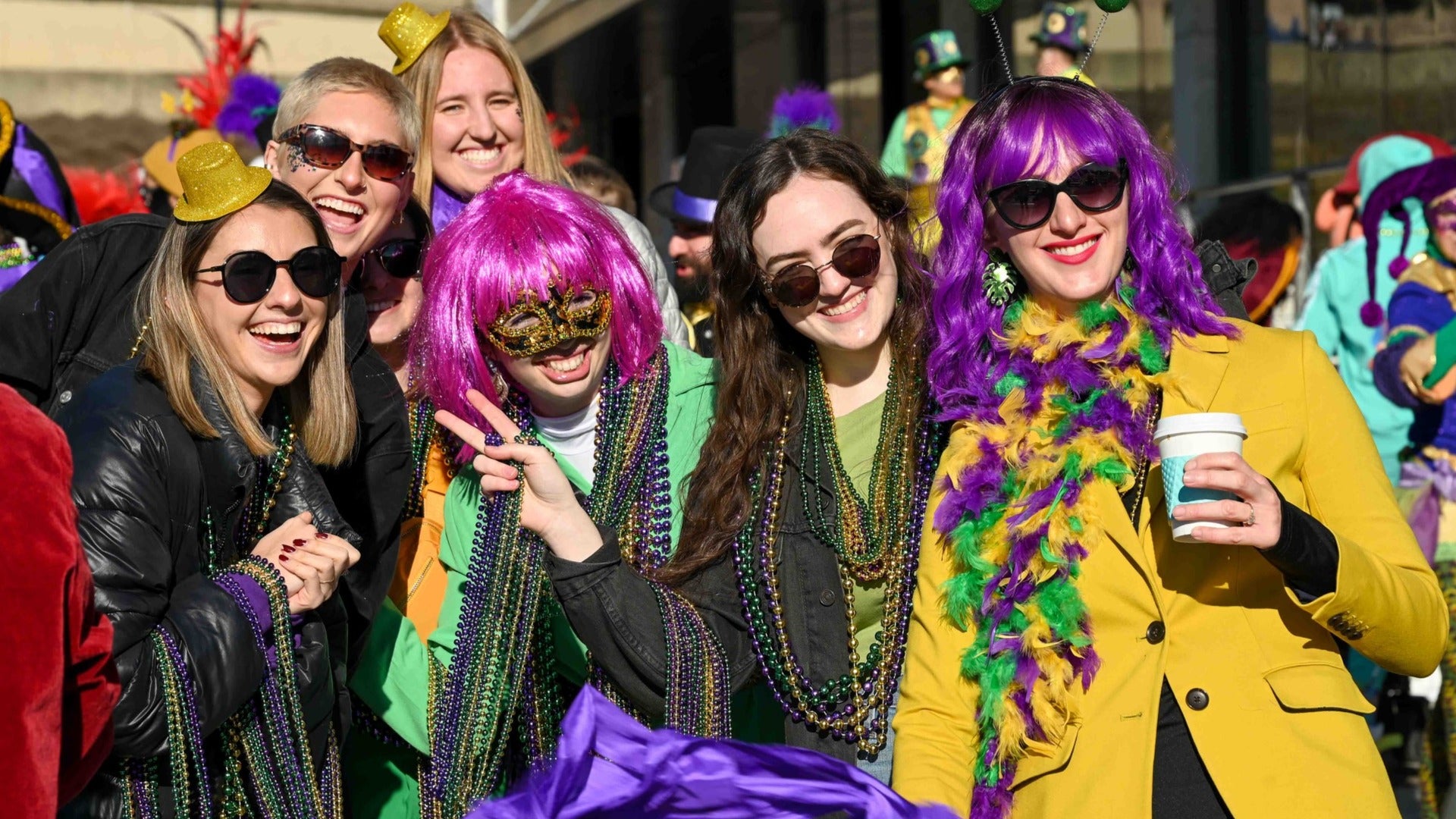 people in mardi gras costumes with a drink and wigs