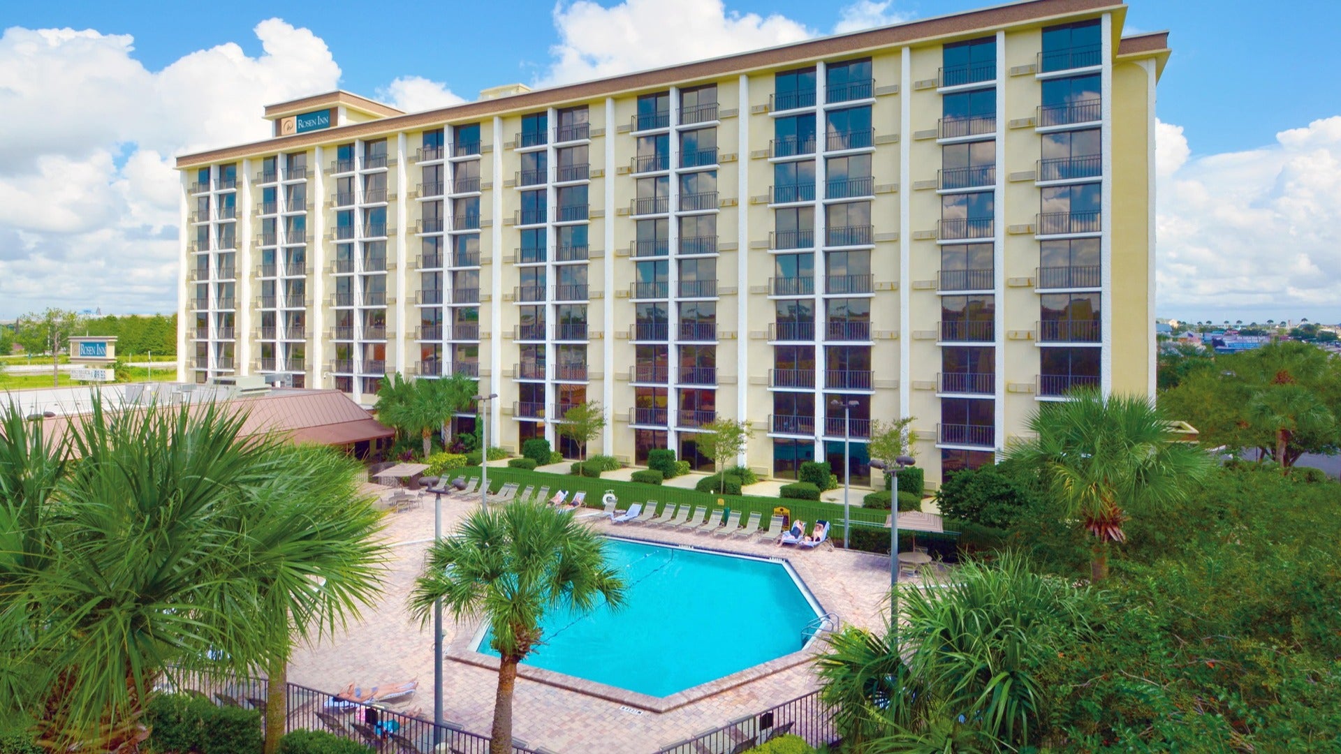 hotel with pool in front, pool chairs, and trees