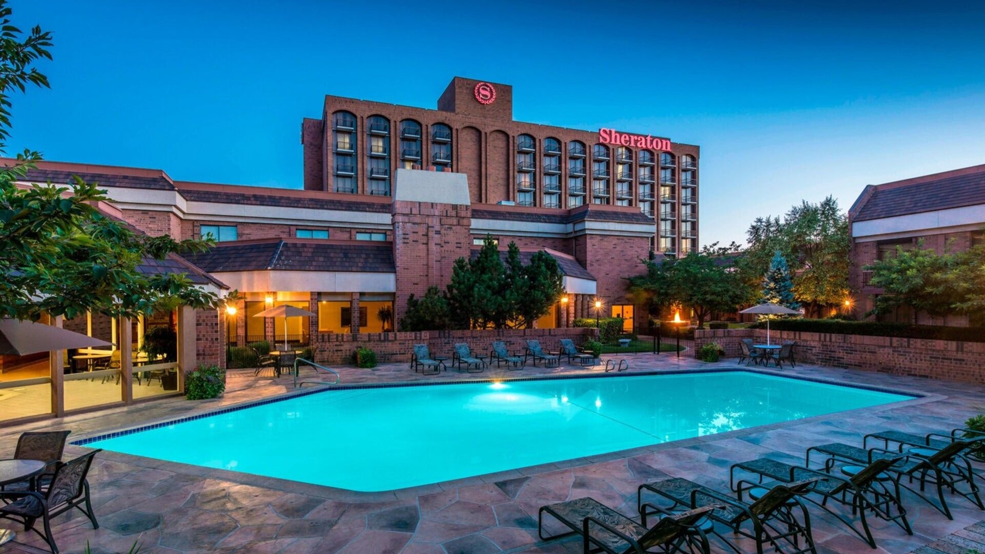 hotel exterior with pool, pool chairs, and trees surrounding it