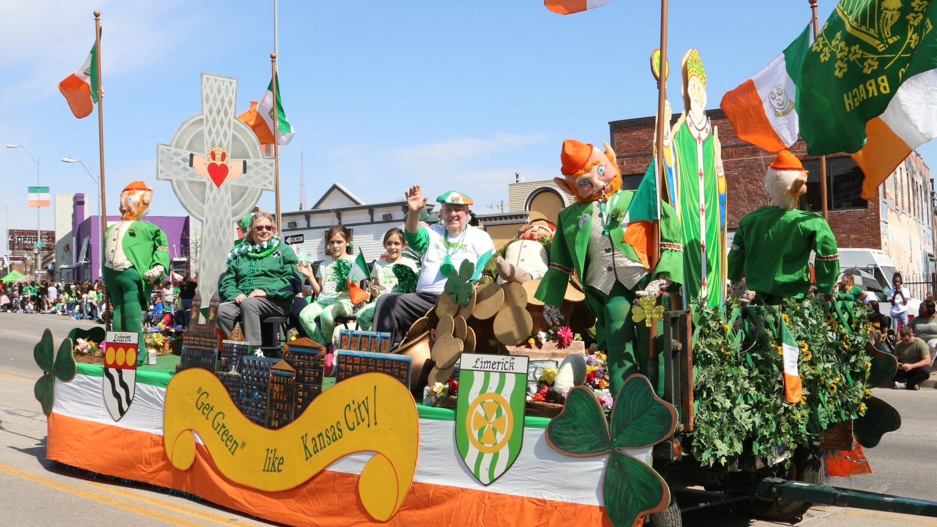 st patricks day parade float with people riding it and irish decor, crowd at the back