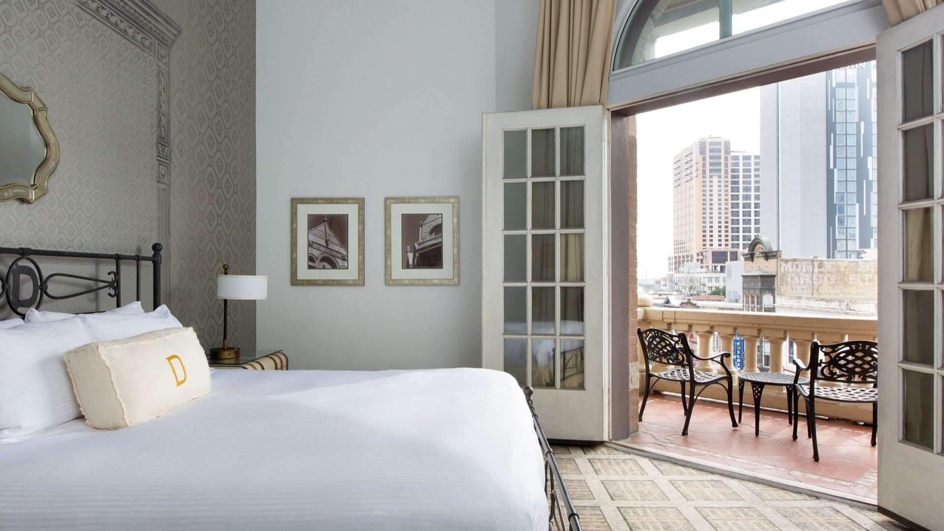 hotel room with bed, mirror, paintings, and balcony with chairs