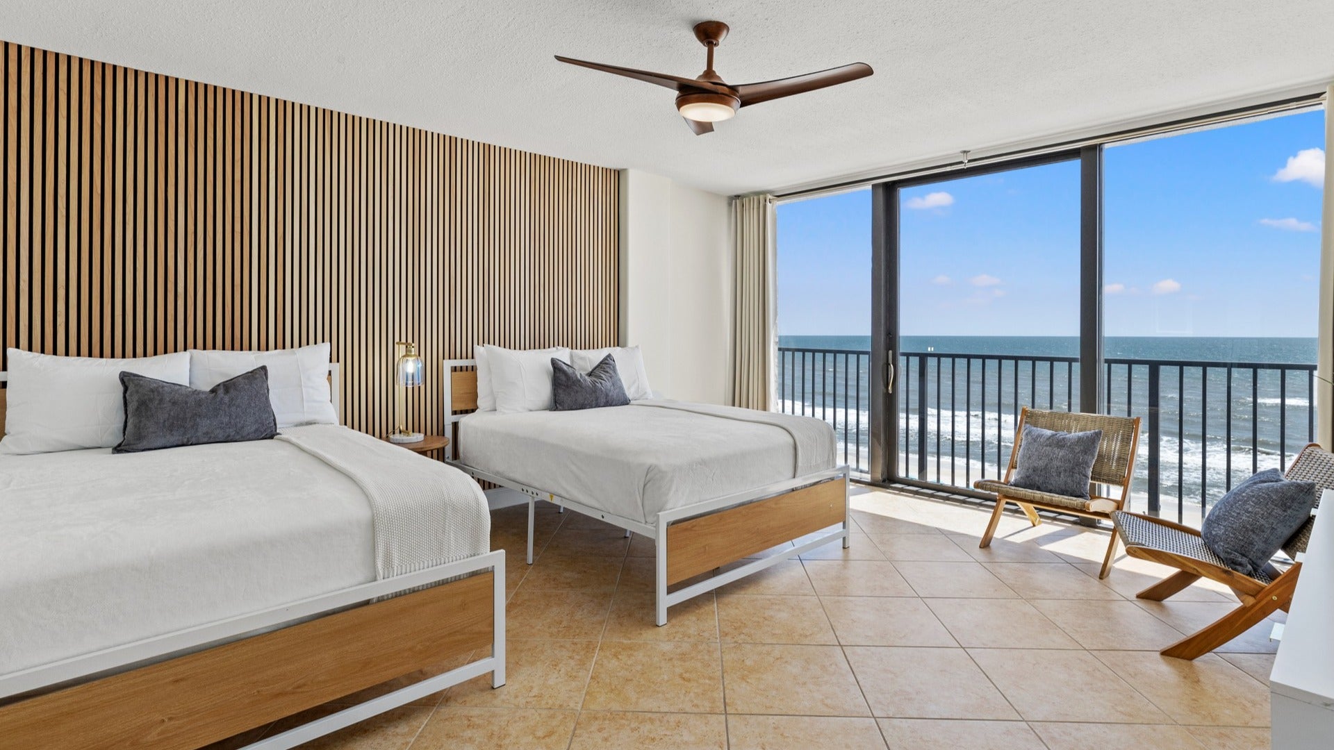 hotel room with beds, lamp, and big window with chairs and view of the ocean