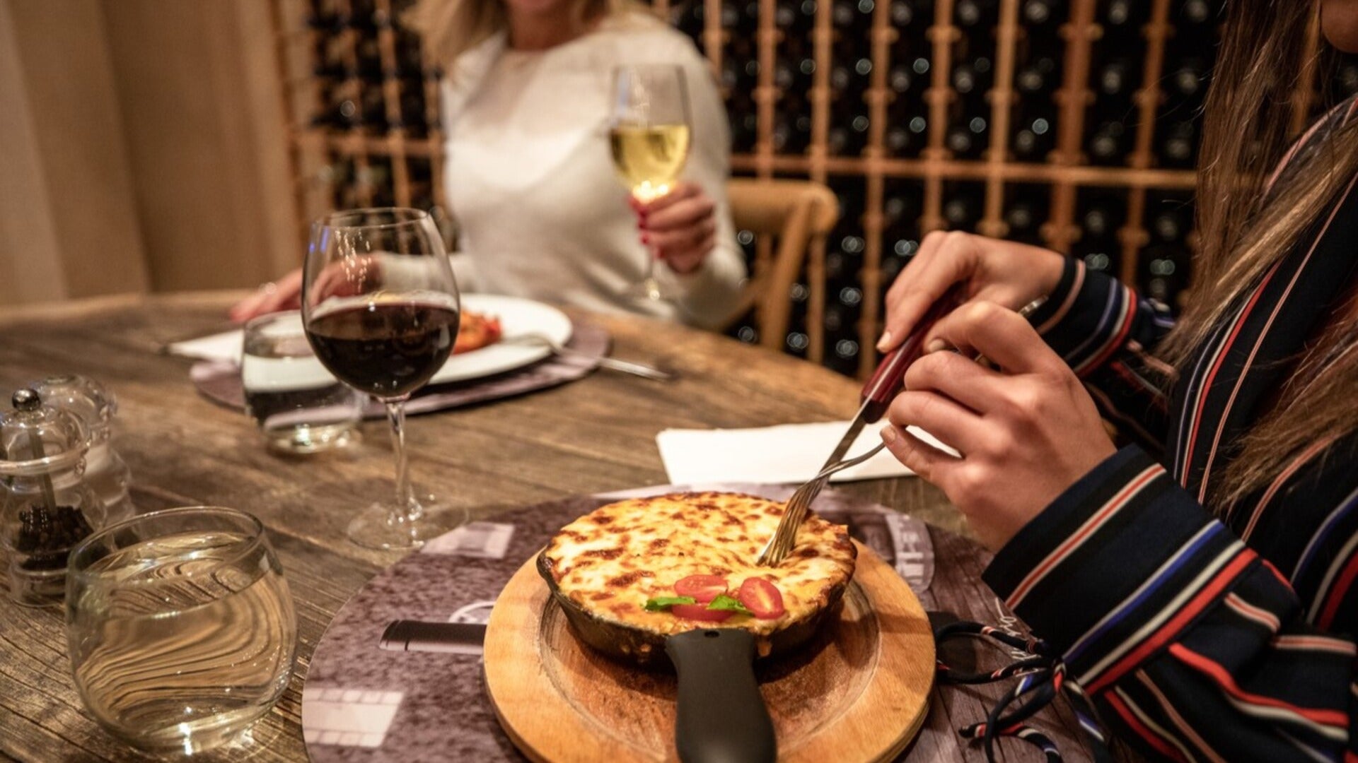 deep dish food item with wine, enjoyed by two girls