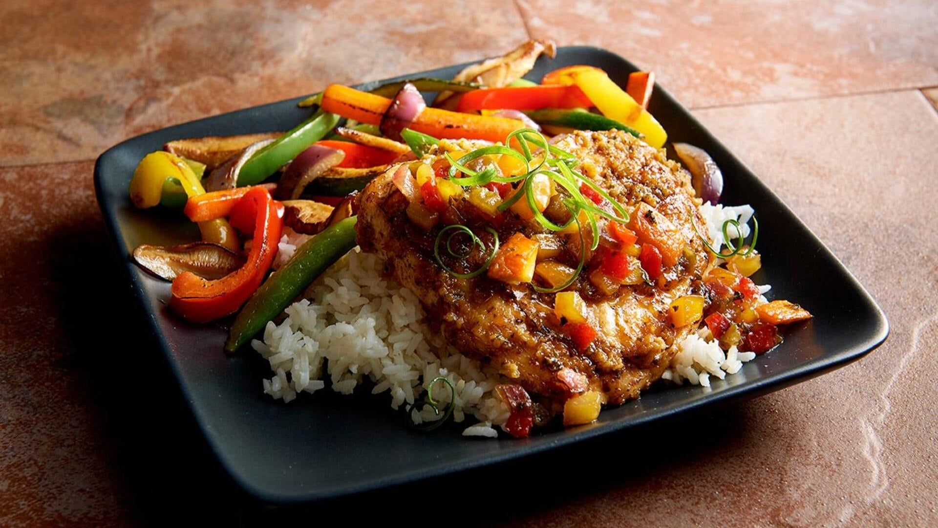 meat with veggies on a bed of rice, served on a plate