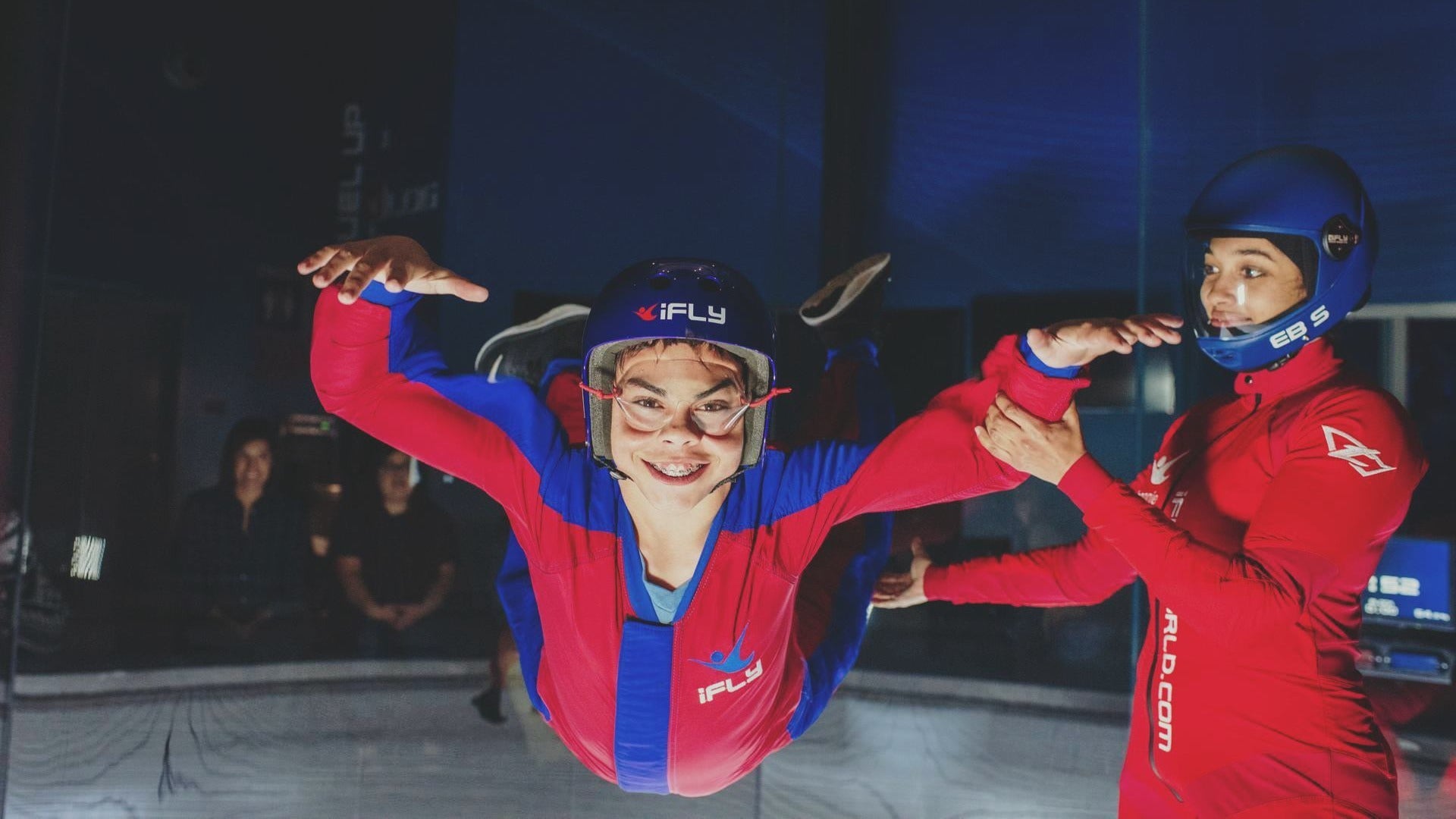 person going indoor skydiving with an instructor holding him