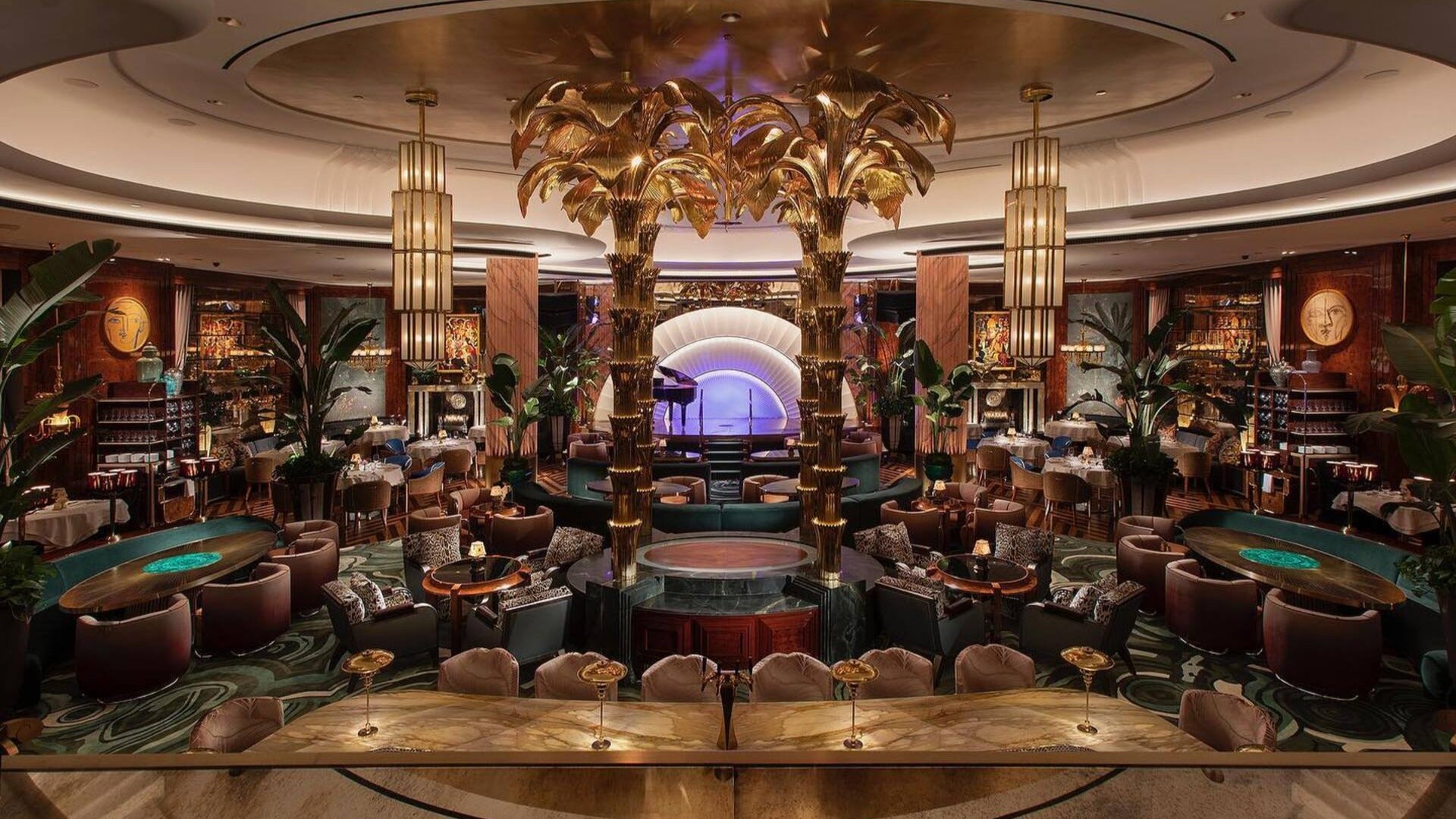 restaurant interior with stage, plush seating, gold chandeliers, alcohol on shelves