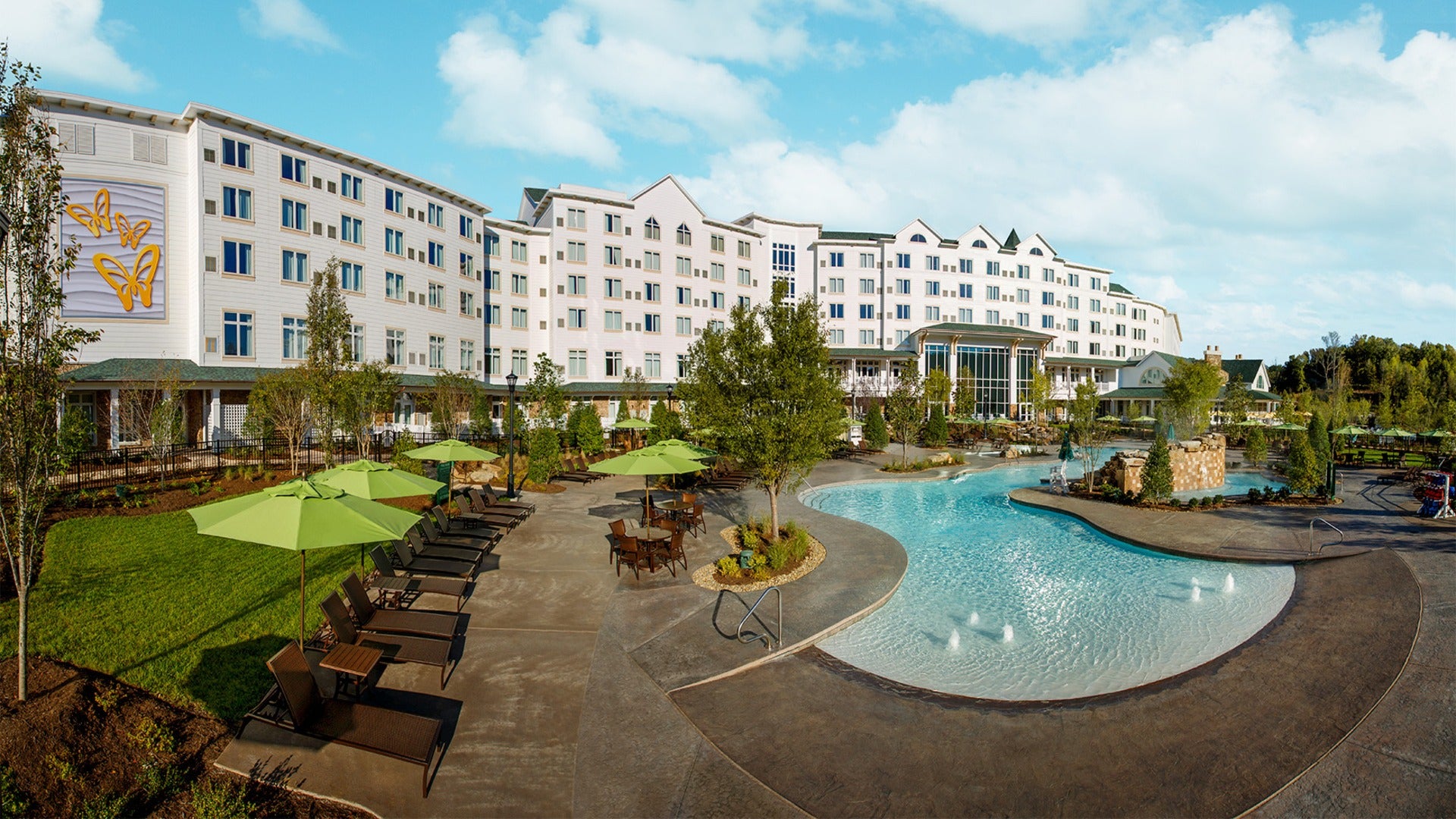 hotel exterior with pool and pool chairs, trees all around