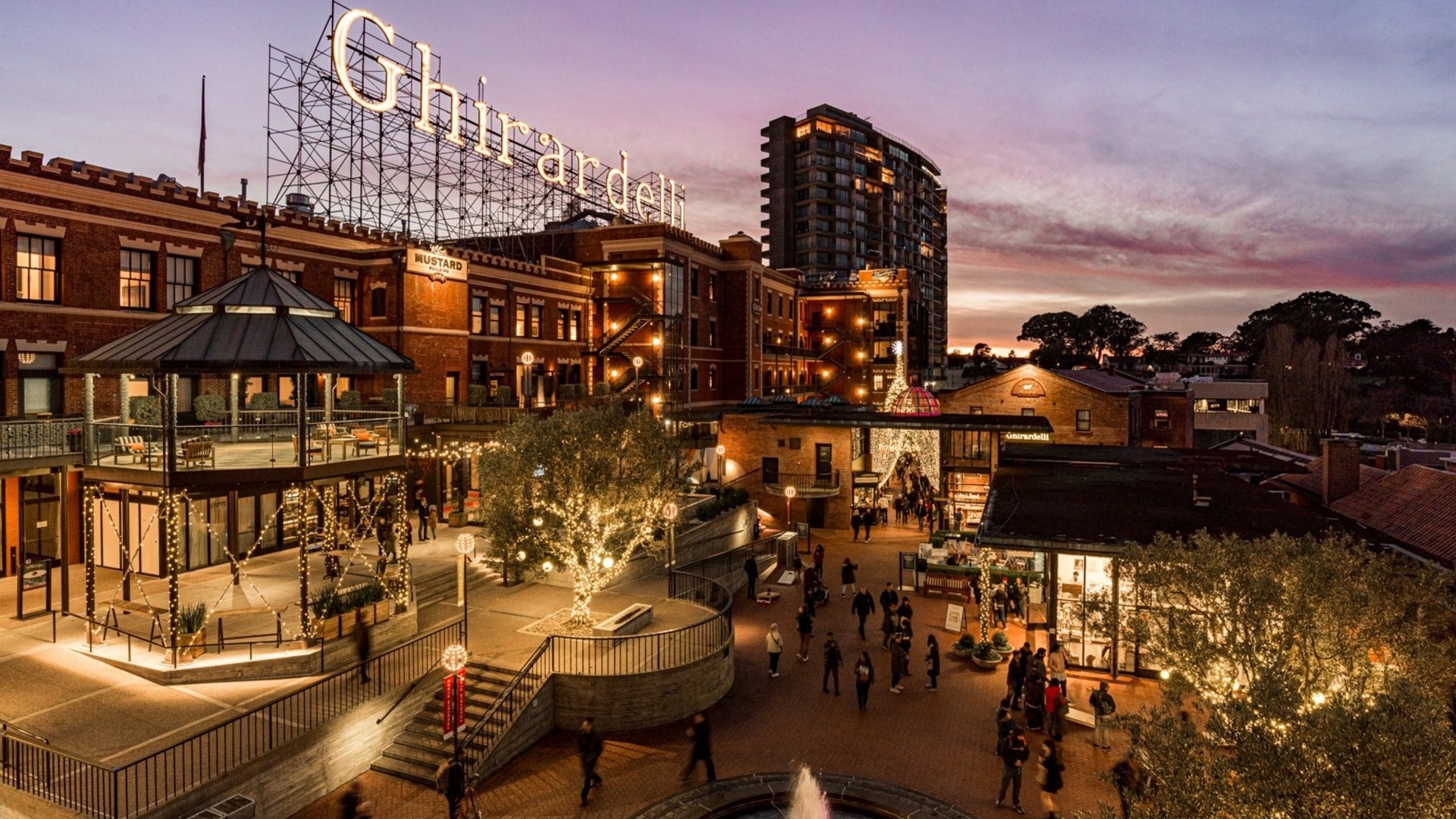 buildings with shopping areas and people walking around, trees with holiday lights