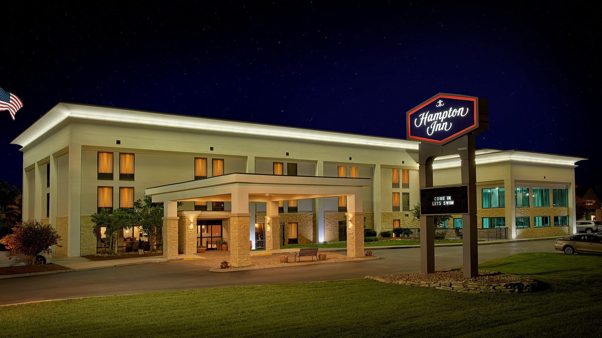 hotel exterior with signage, cars parked, bench at entrance