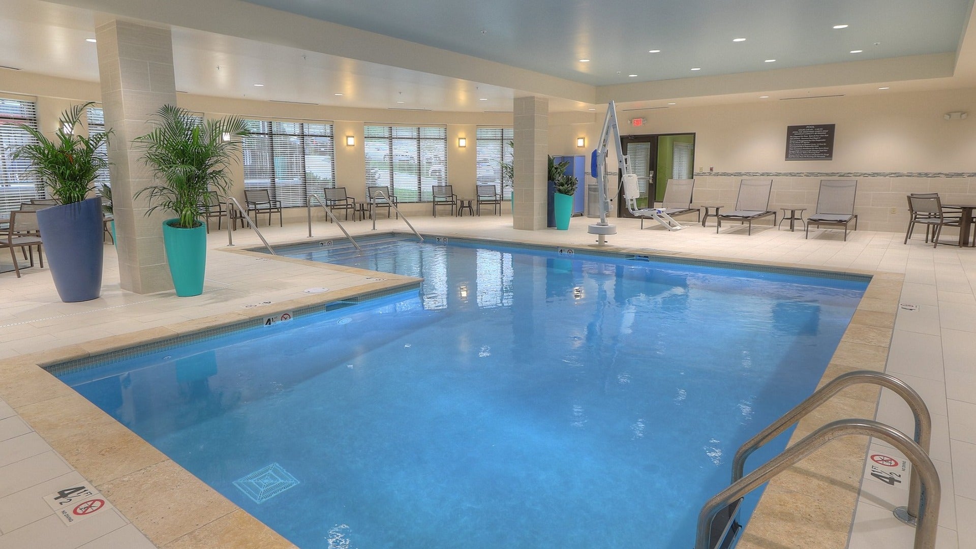 indoor pool with pool chairs on the side and a plant, big windows at the back