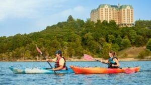couple kayaking on a lake with view of trees and chateau on the lake at the back