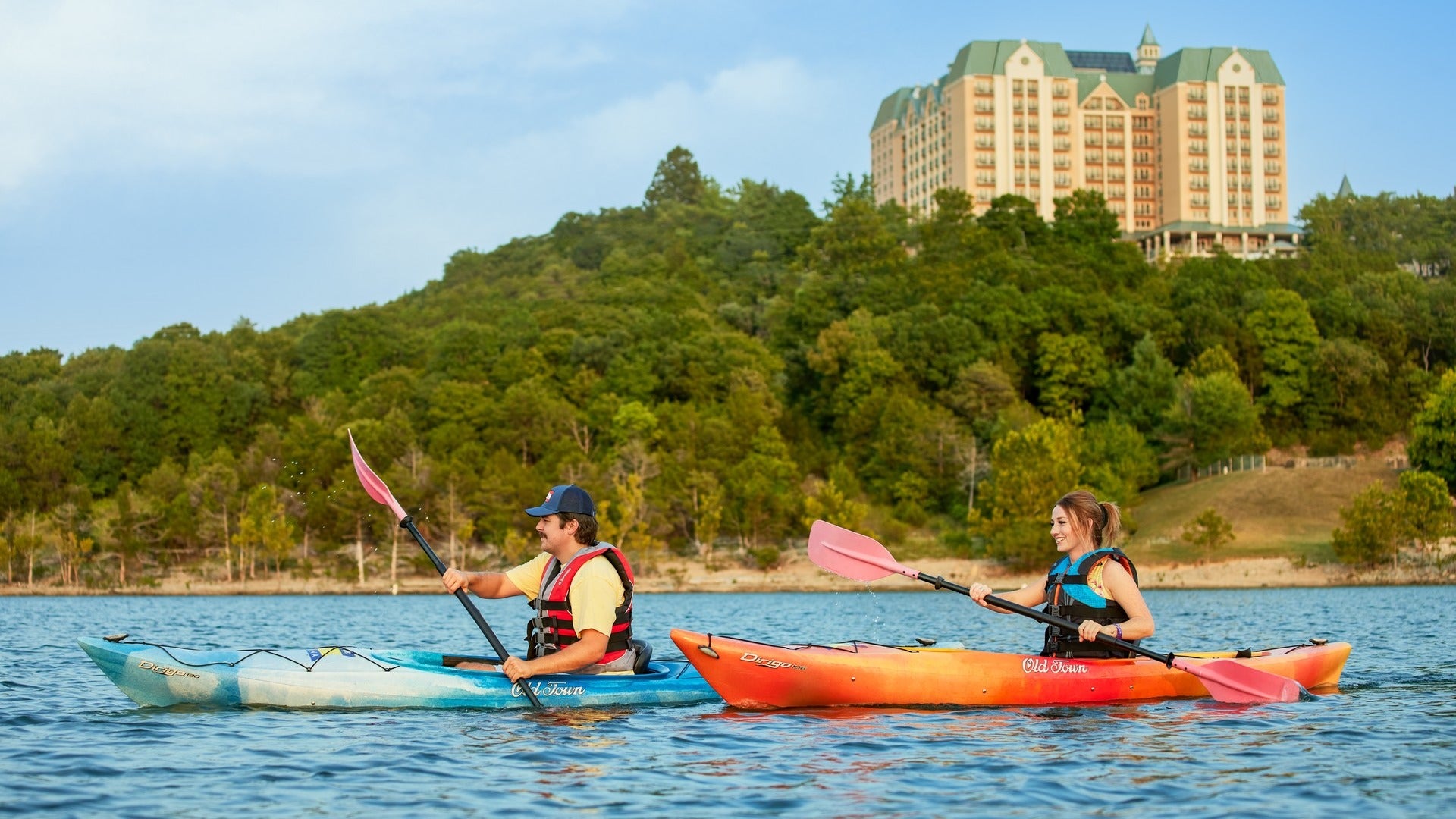 couple kayaking on a lake with view of trees and chateau on the lake at the back