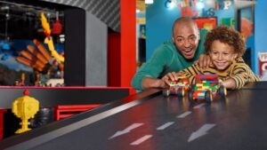 father and son playing with lego cars, road track and lego figures at the back