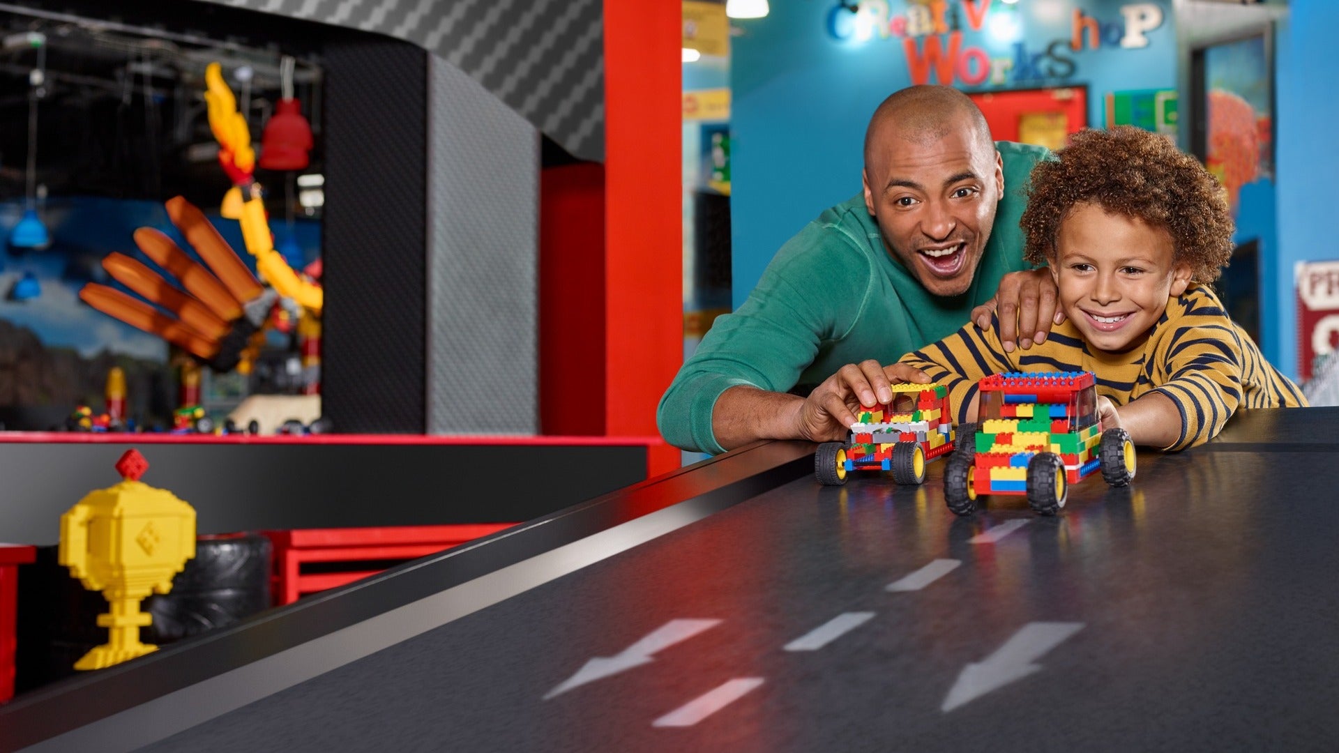 father and son playing with lego cars, road track and lego figures at the back