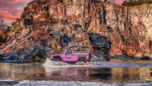 pink jeep passing by a river with rocks behind