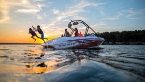 children jumping off a boat with adults watching on a lake