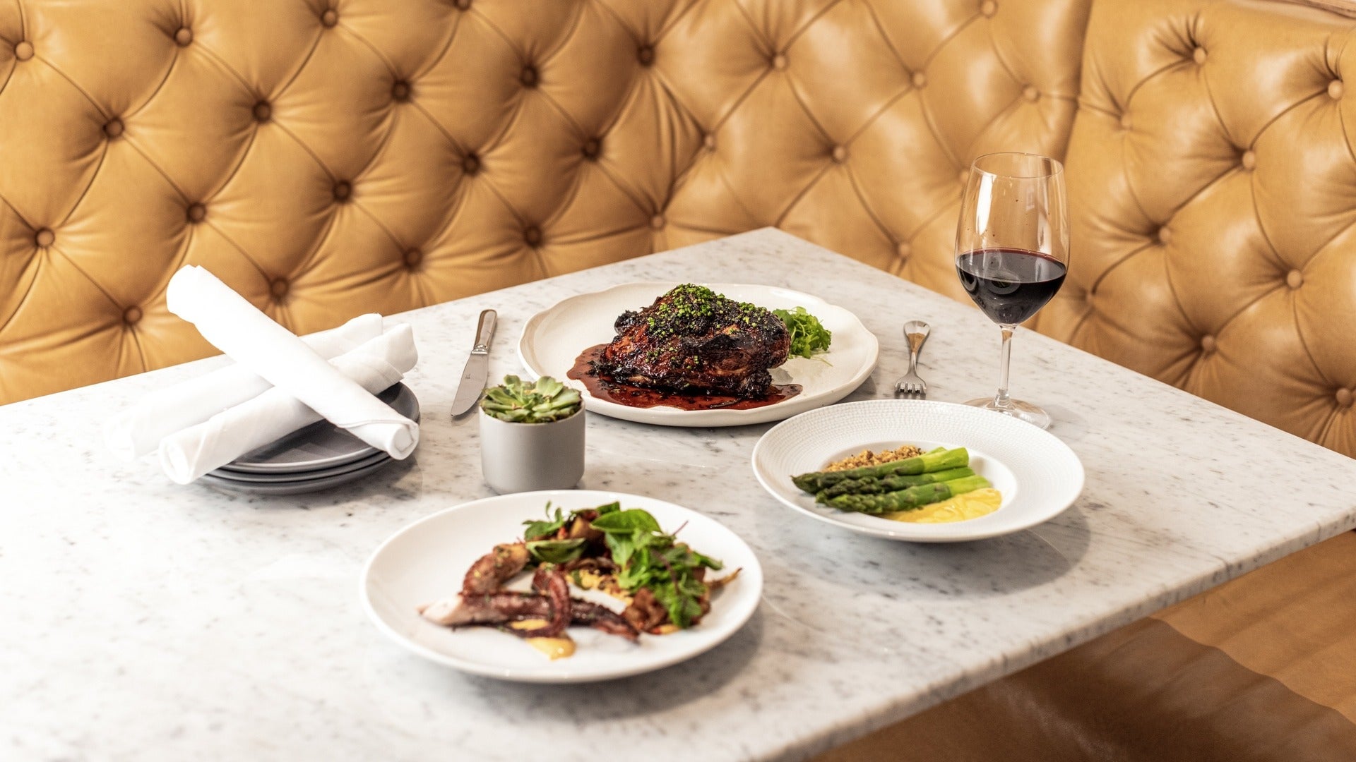 steak, arugula, wine, and other dishes on a table, cutleries and plates on the side