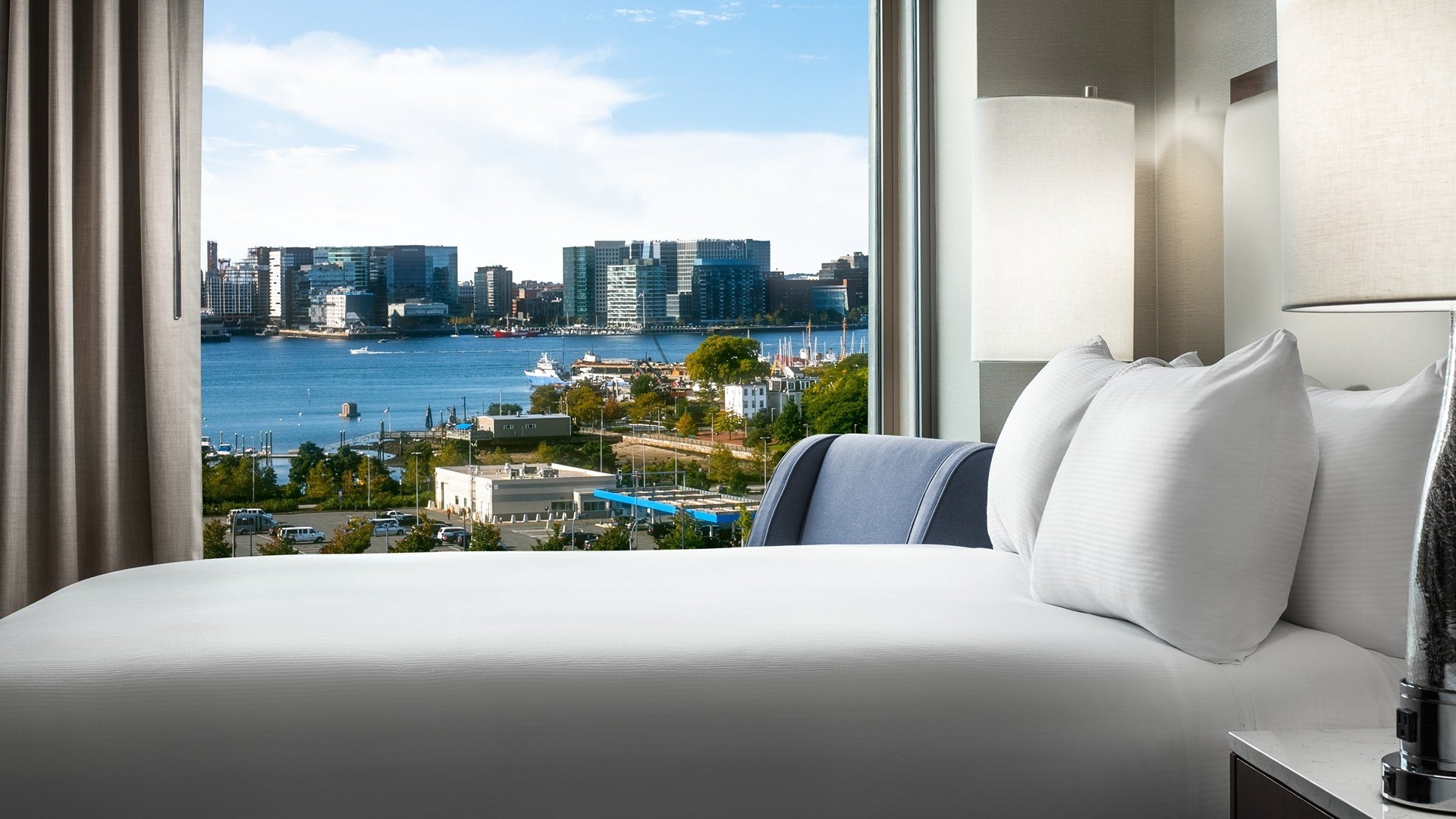 hotel room with a bed, lamp, pillows, chairs, and view of boston skyline