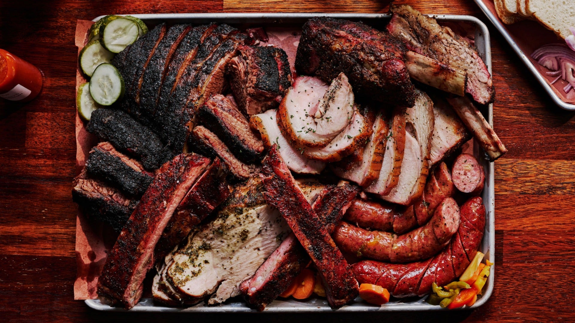 various meats on a platter with veggies on the side and sausages