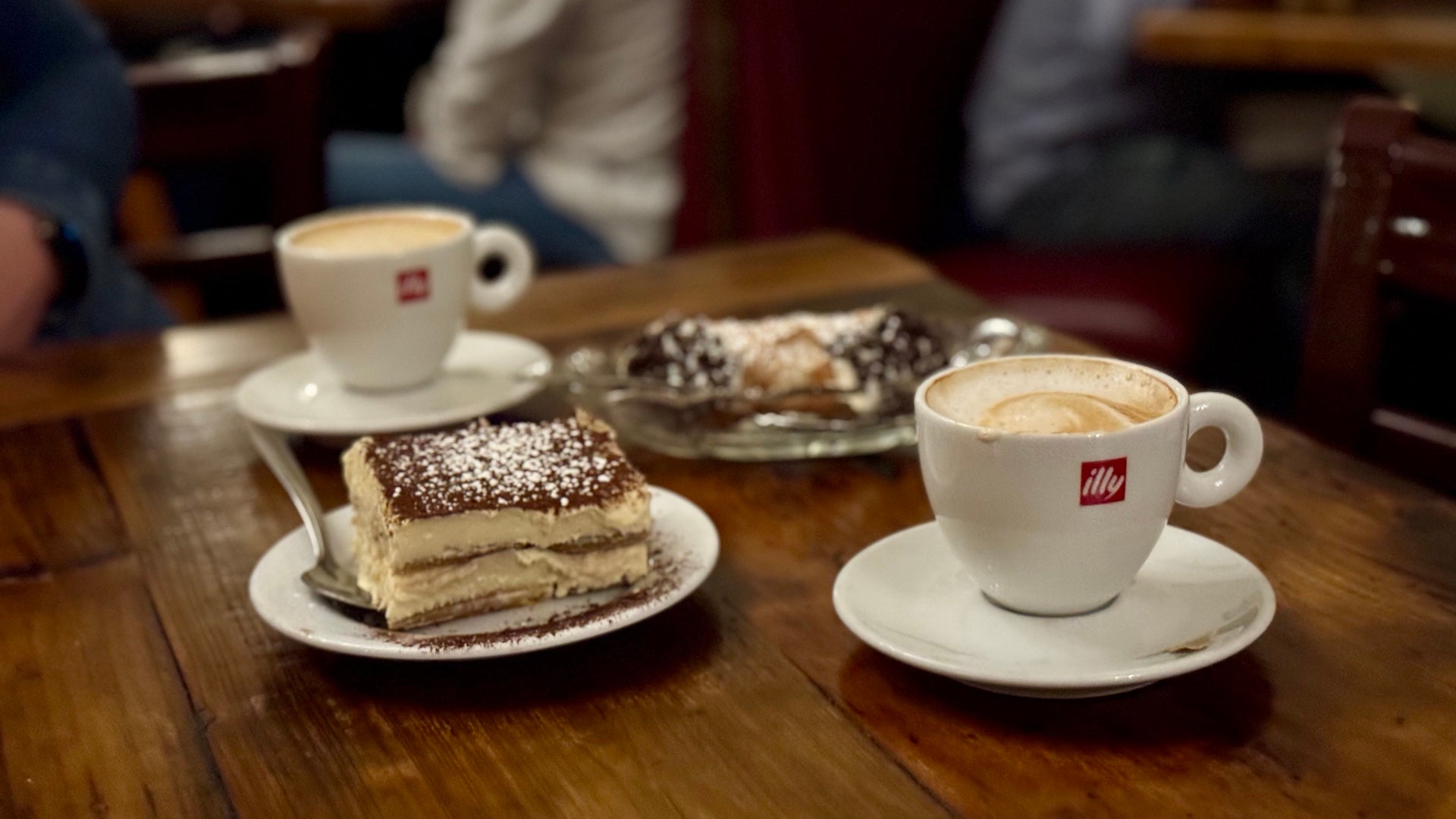 Tiramisu, coffees, and a cannoli on a table in an Italian restaurant