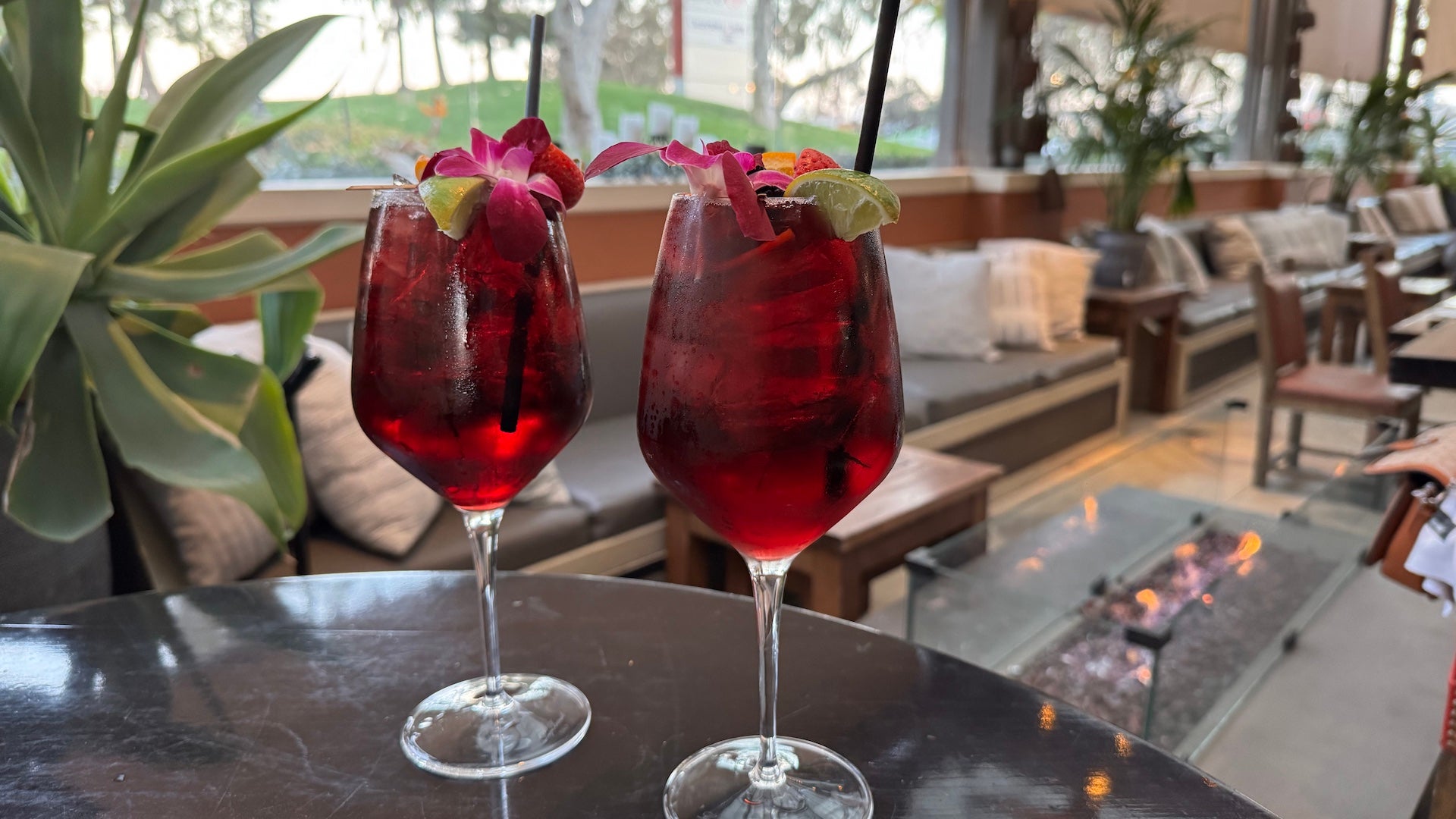 Two red sangrias on a table with couches and a fireplace in the background