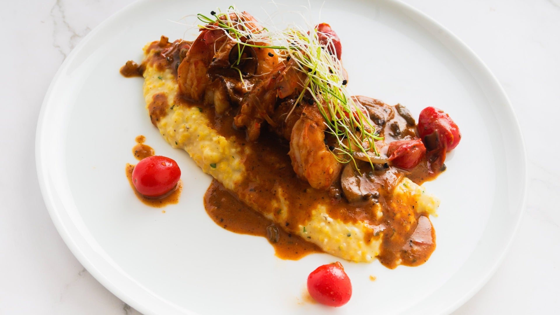 shrimp and grits served on a plate with a side of tomatoes