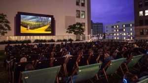 people watching at an outdoor movie theater with buildings on the side