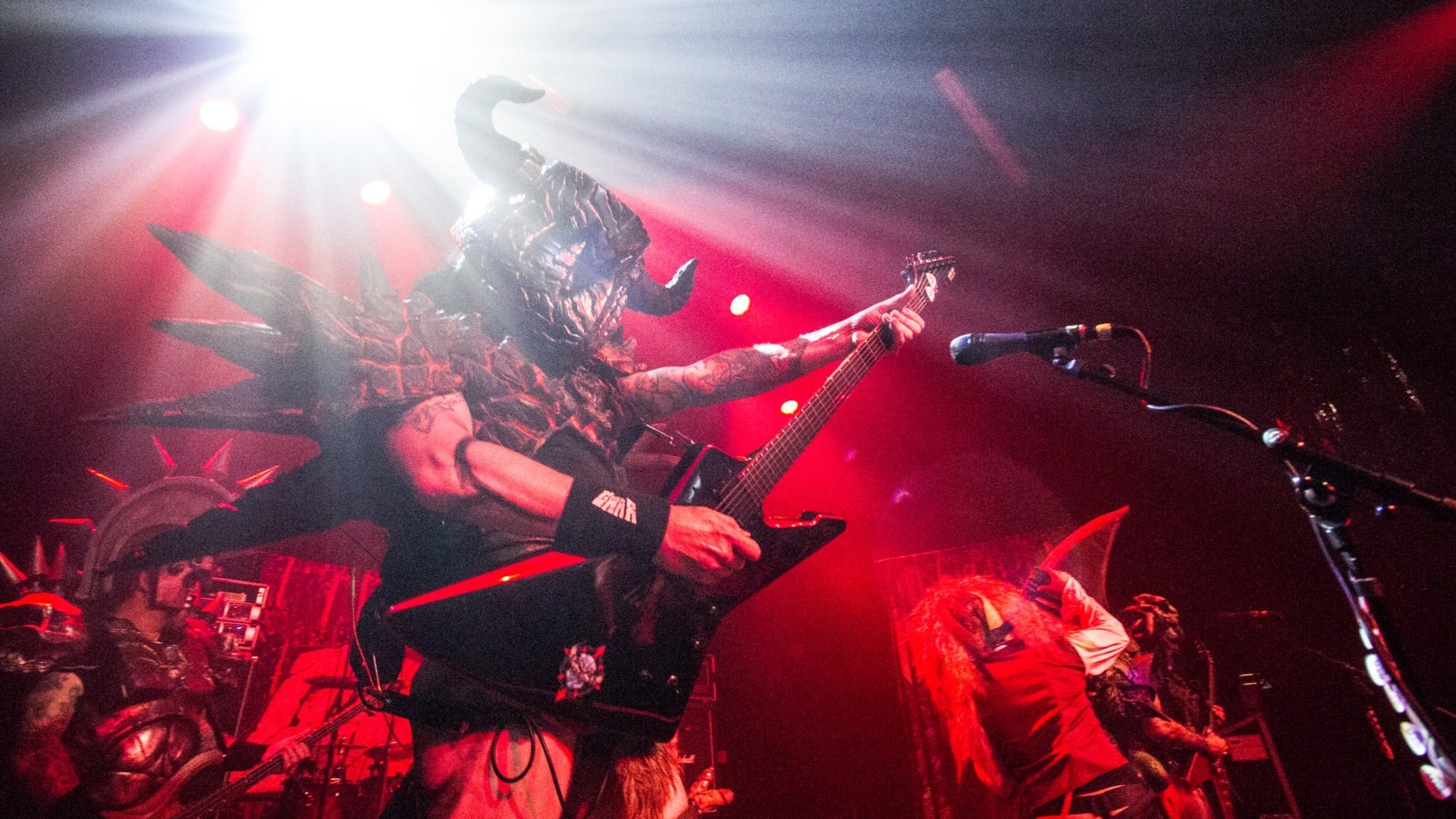 performer on stage wearing a mask and holding a guitar with a microphone stand