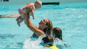 woman holding a baby up with kids swimming around her