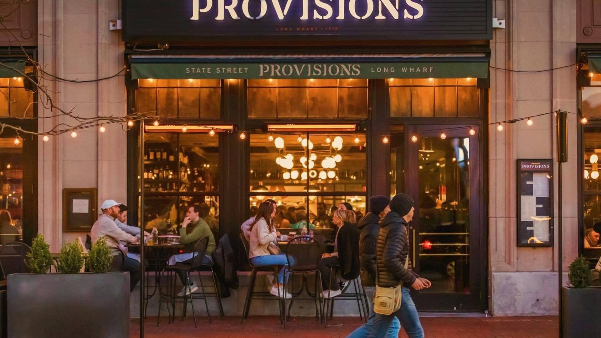 people walking by a restaurant with people eating in it