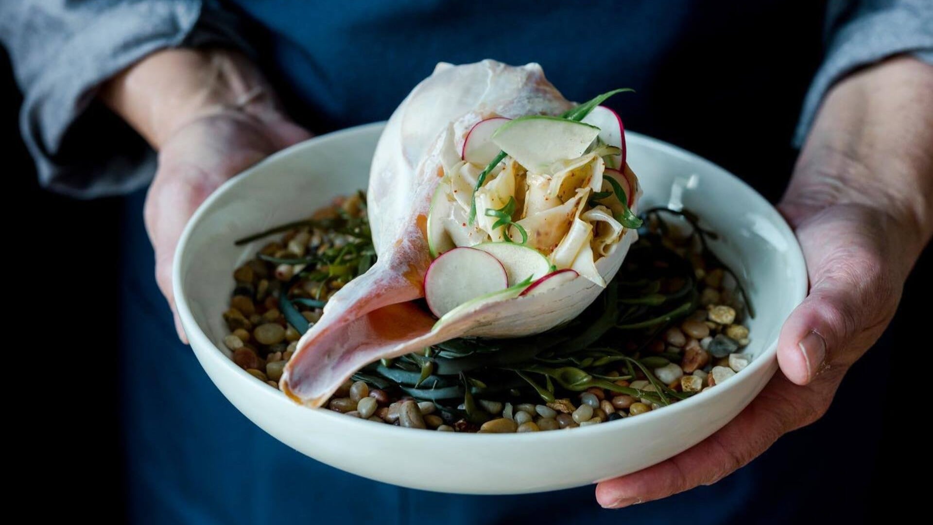 man holding a salad served in a conch plate