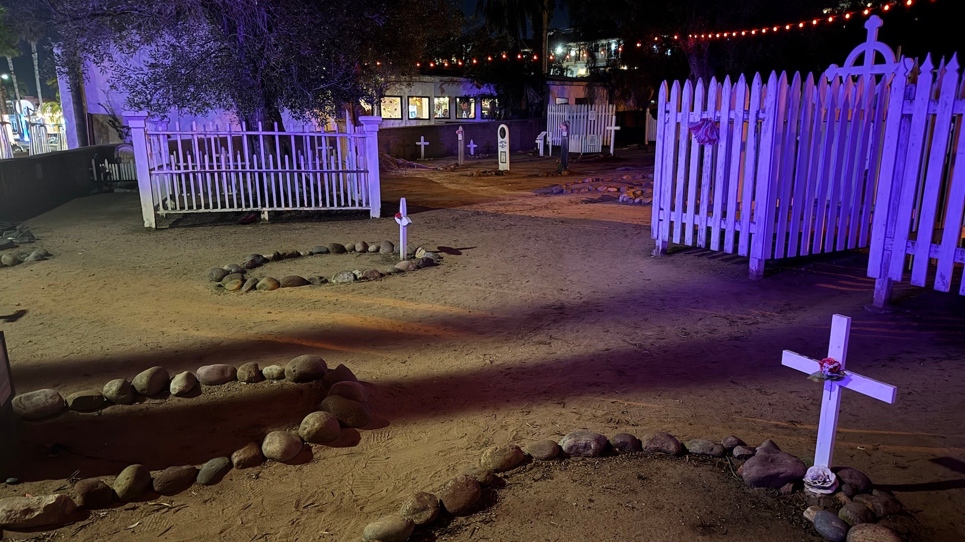 Dimly lit graveyard with white fencing and white crosses