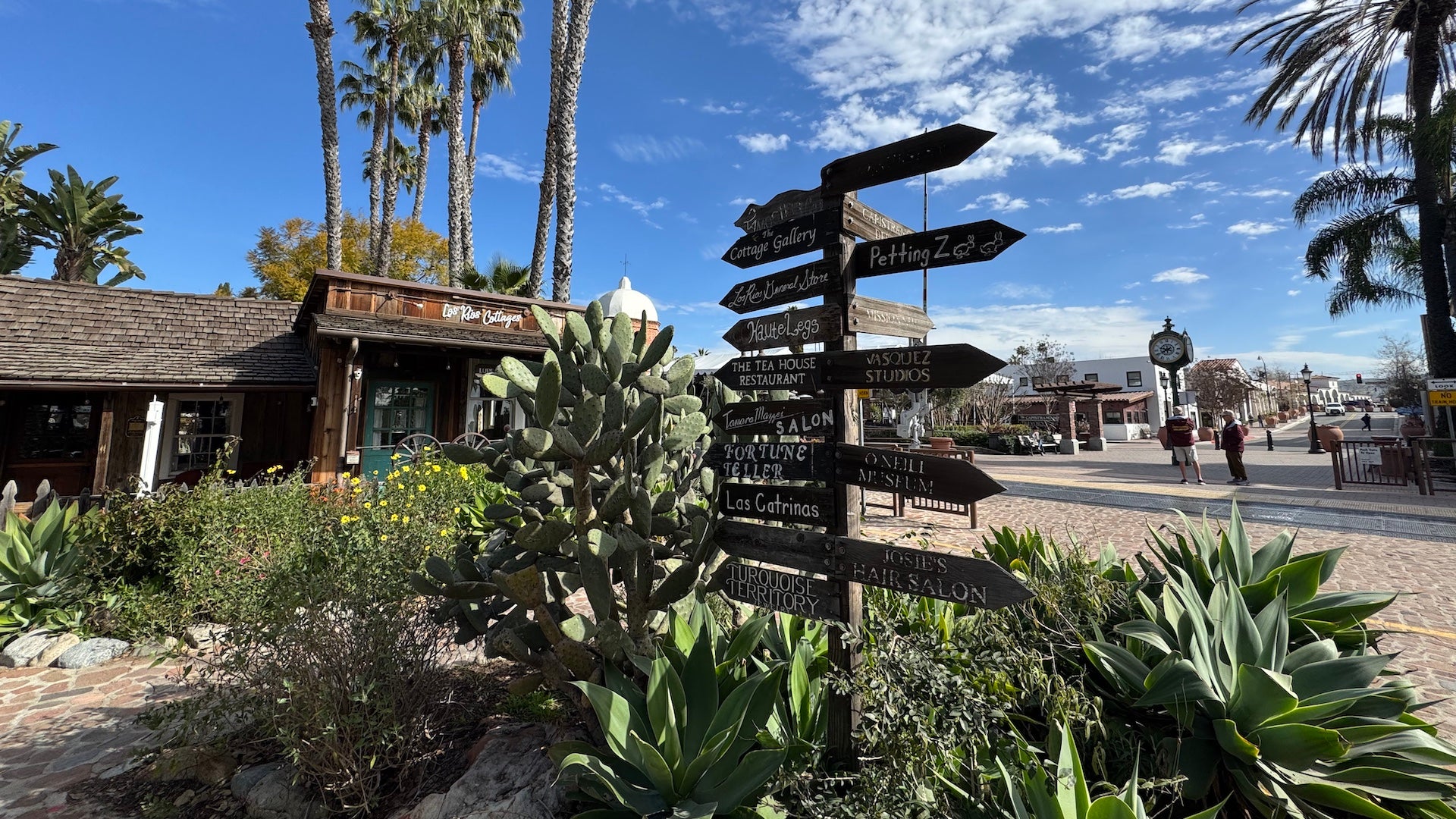 Wooden signs in a garden with a old wooden building behind it under a blue sky