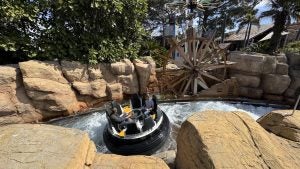 Visitors riding the Shipwreck Rapids water ride surrounded by rocky cliffs and a waterwheel at SeaWorld San Diego.
