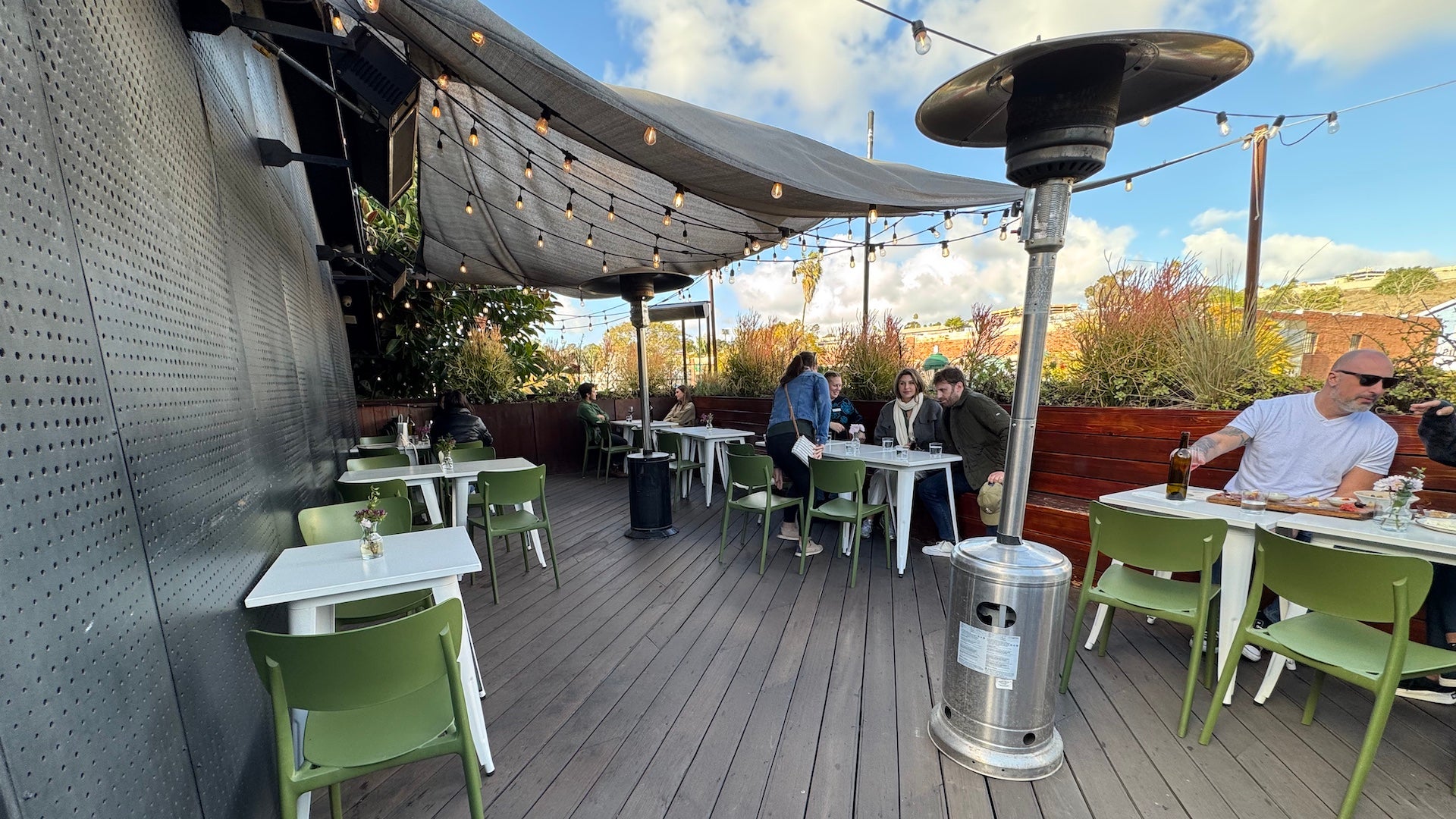 Outdoor patio with hanging lights, green chairs, white tables, and a heat lamp