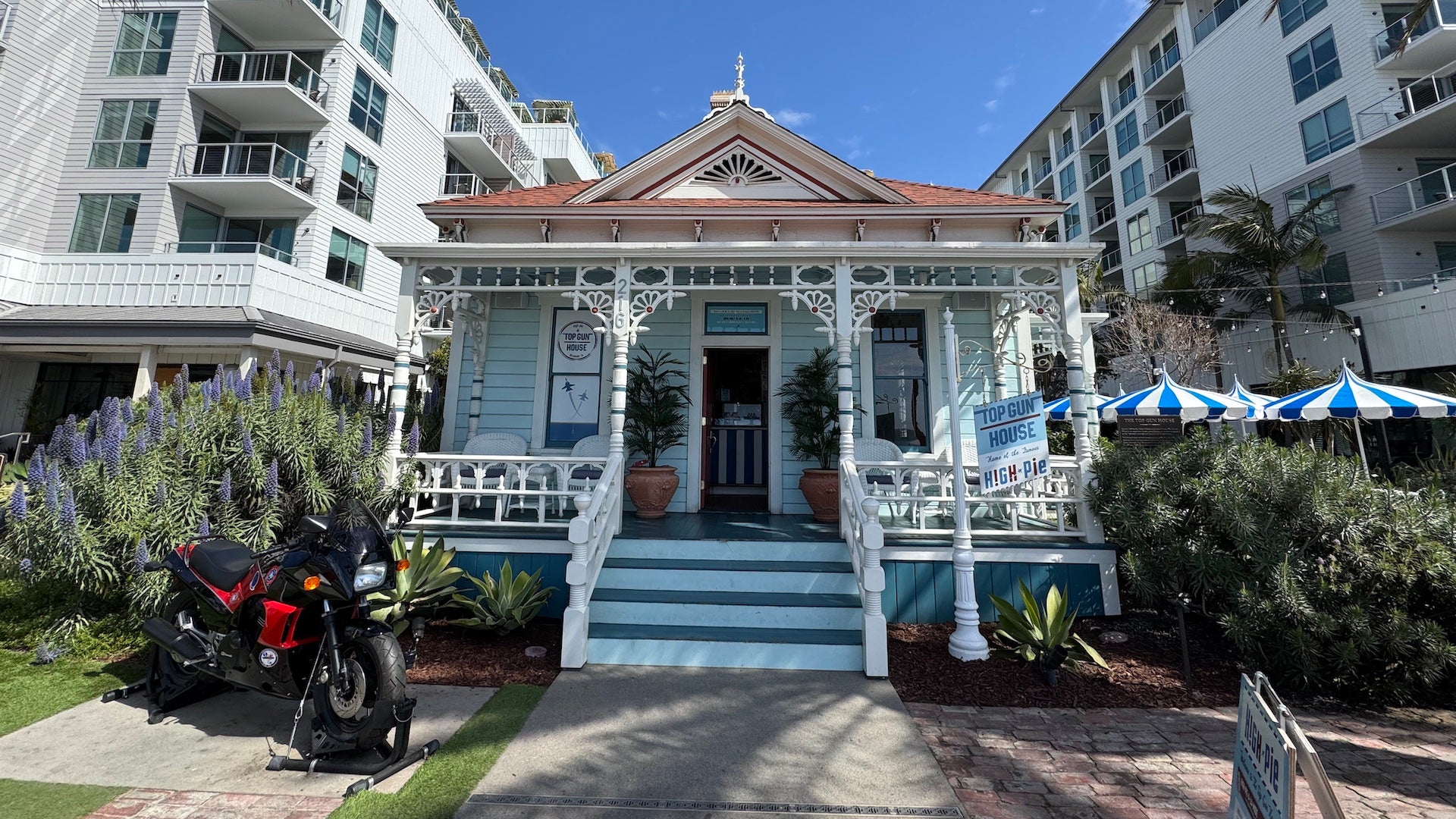 Little blue house with a white front porch and striped umbrellas, there is also a motorcycle parked out front