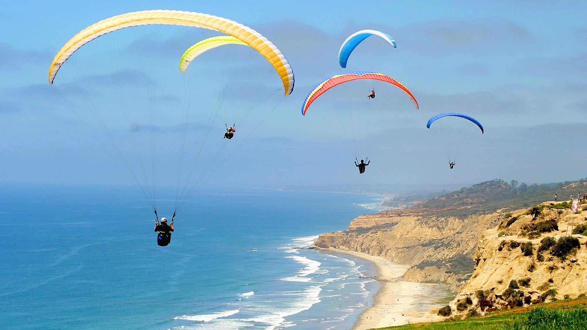 five people paragliding above the beach side
