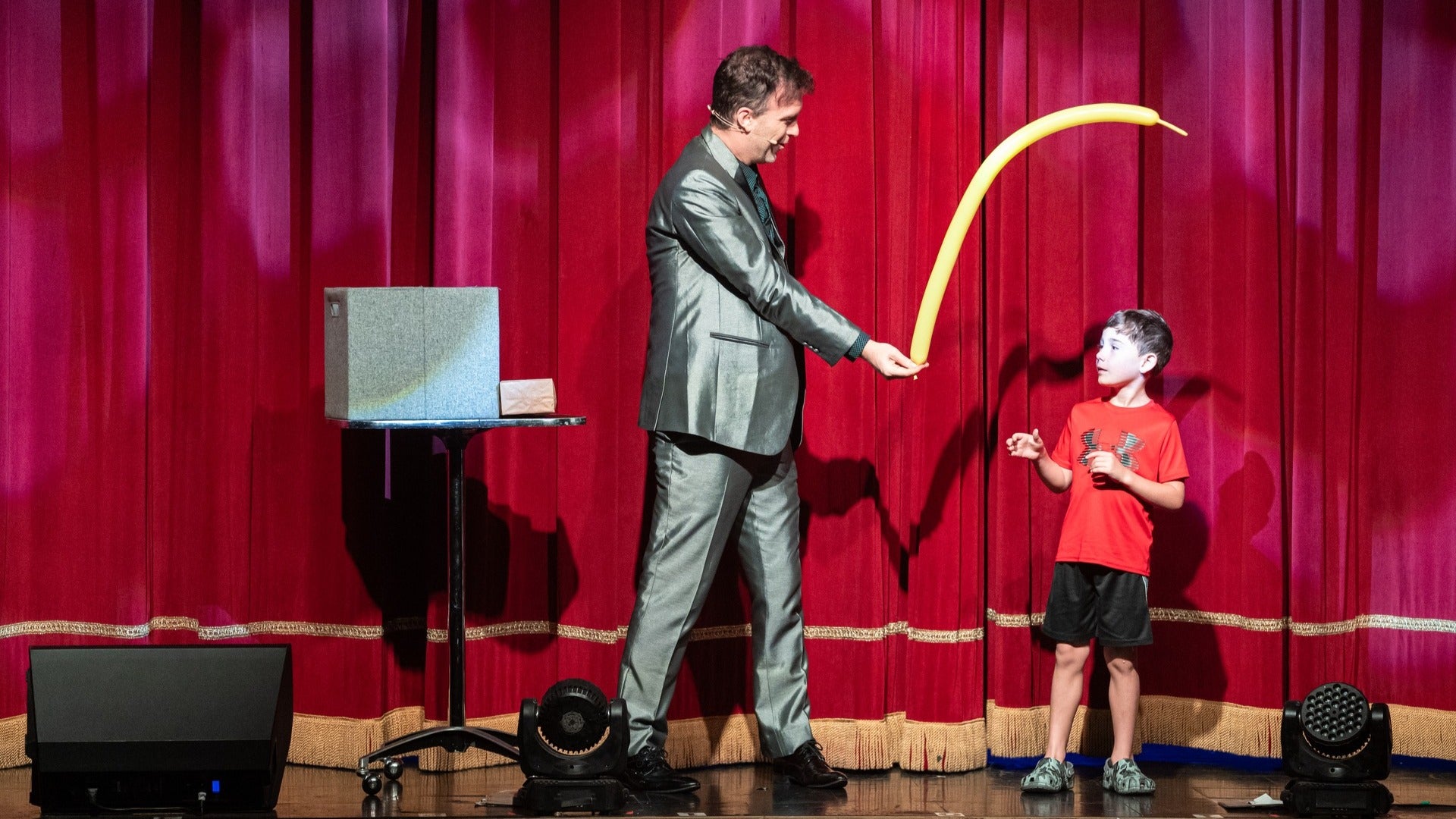 magic performer on stage holding a balloon with a kid