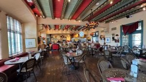 Interior of The Prado at Balboa Park, featuring eclectic vintage decor, colorful painted ceiling beams, iron chandeliers, and an inviting dining area with dark wood floors and bistro-style seating.